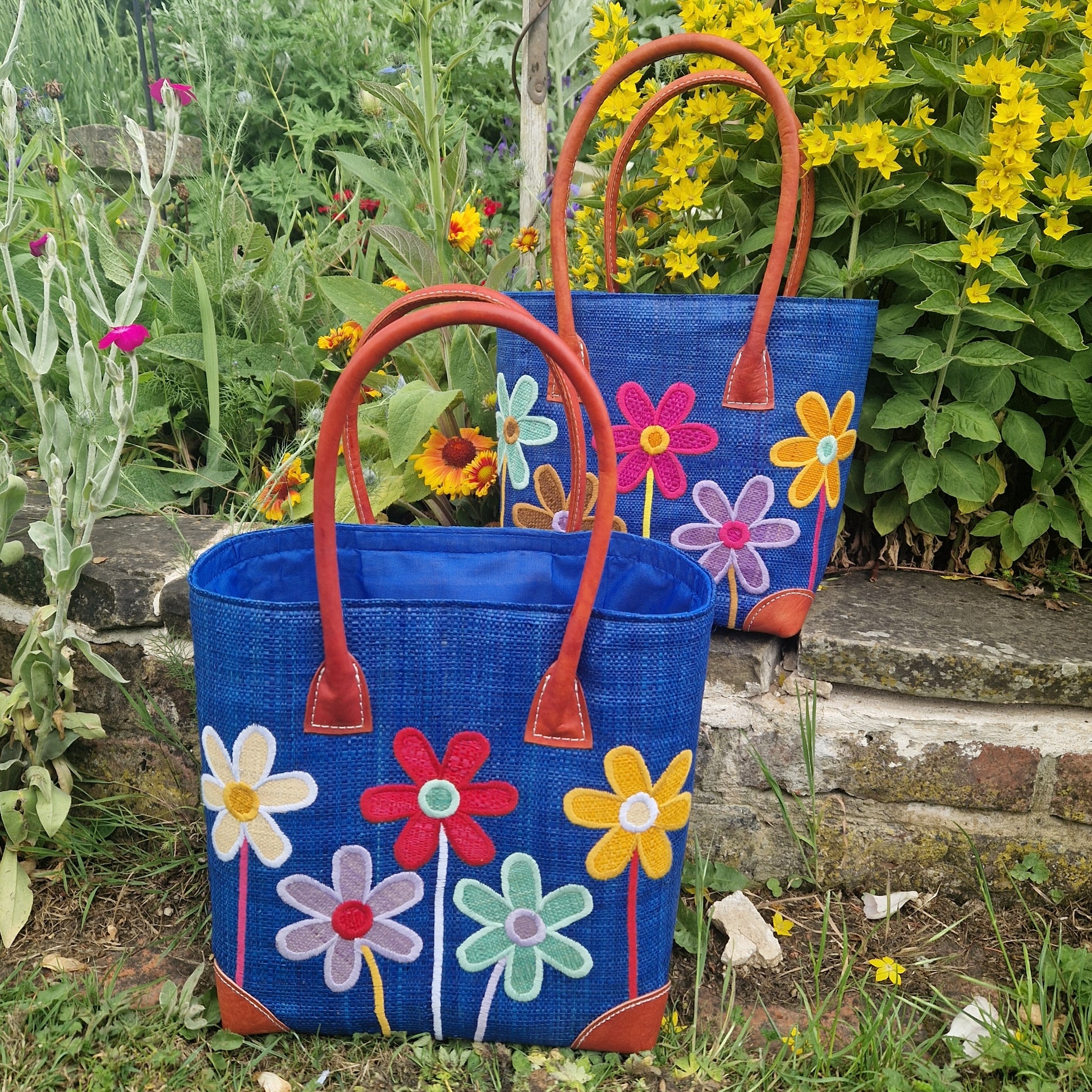 Two blue bags with colorful floral designs on a garden background