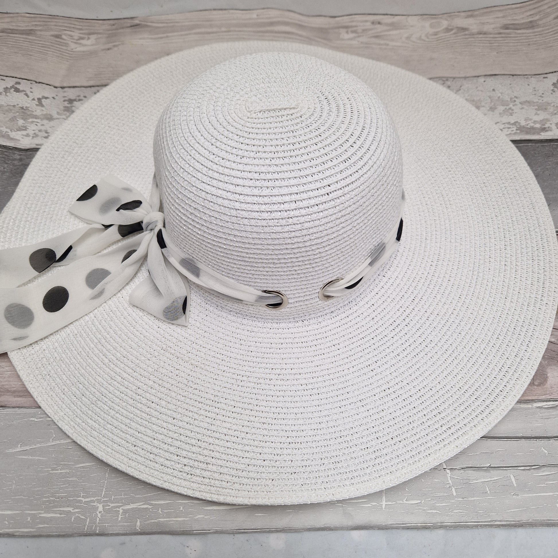 White wide brimmed hat with a white spotted scarf band around it fastened with a bow.