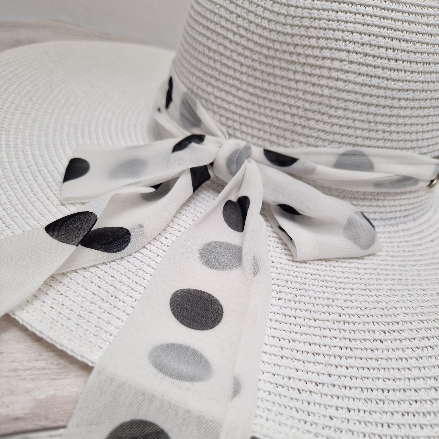 White wide brimmed hat with a white spotted scarf band around it fastened with a bow.