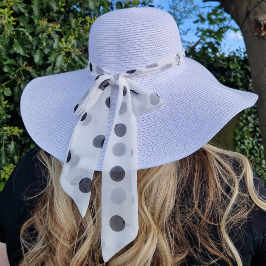 Lady wearing a white wide brimmed hat with a white spotted scarf band around it fastened with a bow.