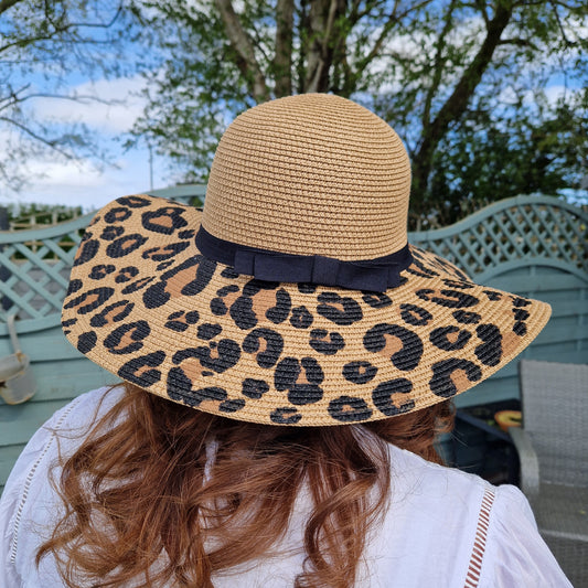 Lady wearing a wide brimmed biscuit coloured hat with leopard print across the brim and a black ribbon band.