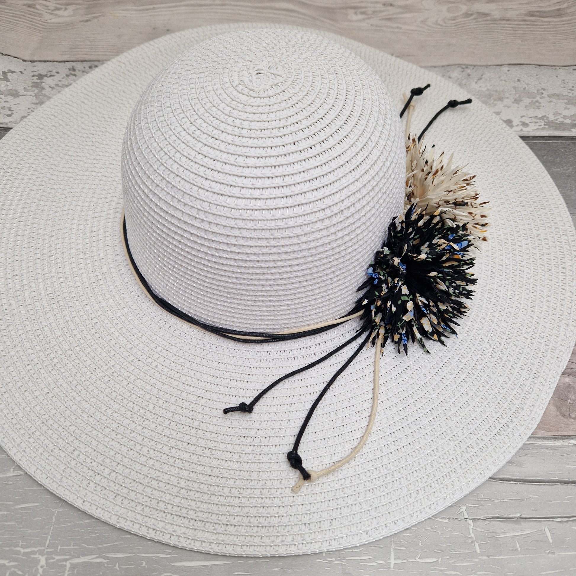 White wide brimmed hat decorated with 2 flowers in black and cream tones.