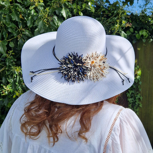 Lady wearing a white wide brimmed hat decorated with 2 flowers in black and cream tones.