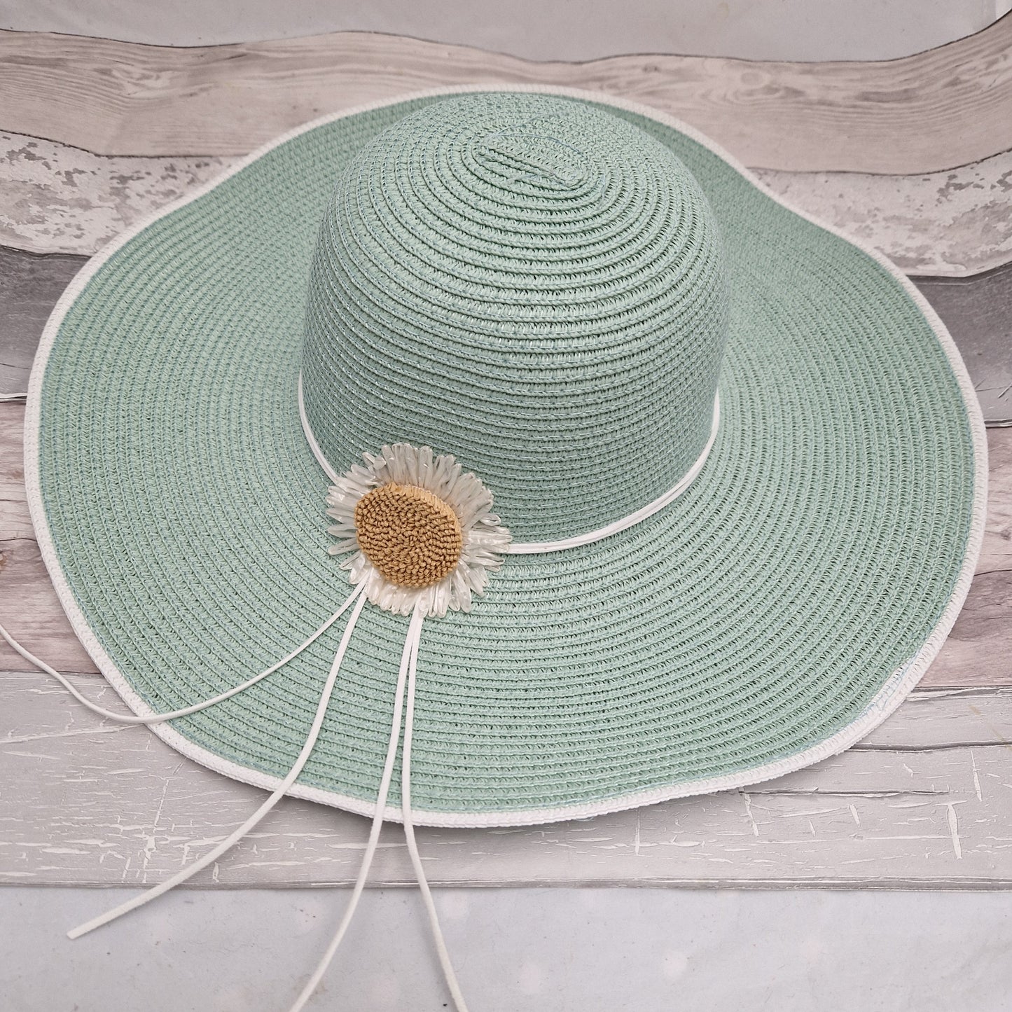 Wide brimmed mint green hat decorated with a daisy flower.