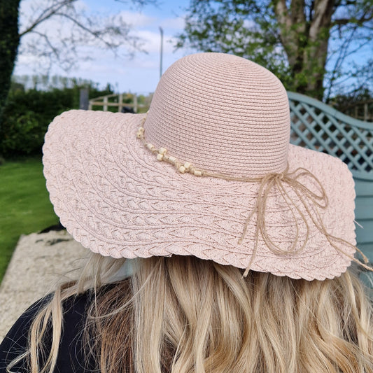Lady wearing a pale pink wide brimmed hat with a beaded band.