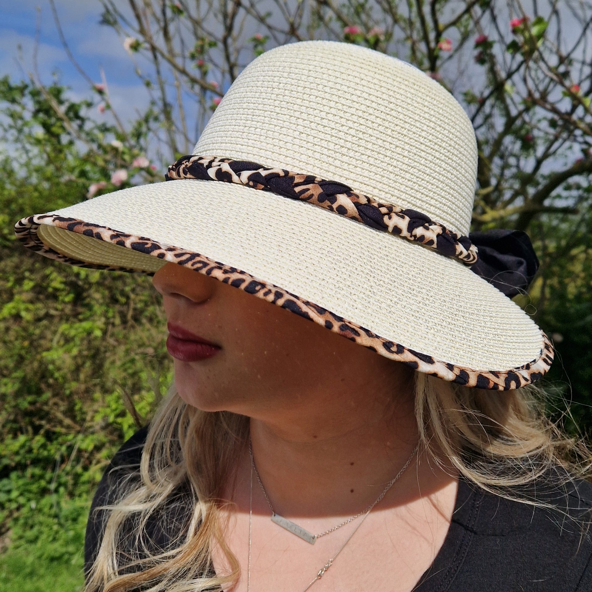 Lady wearing a Cream open backed hat with an animal print trim and black bow.