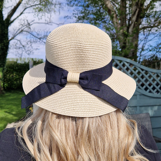 Natural coloured Cloche style hat with a wide black band finished with a bow at the back.