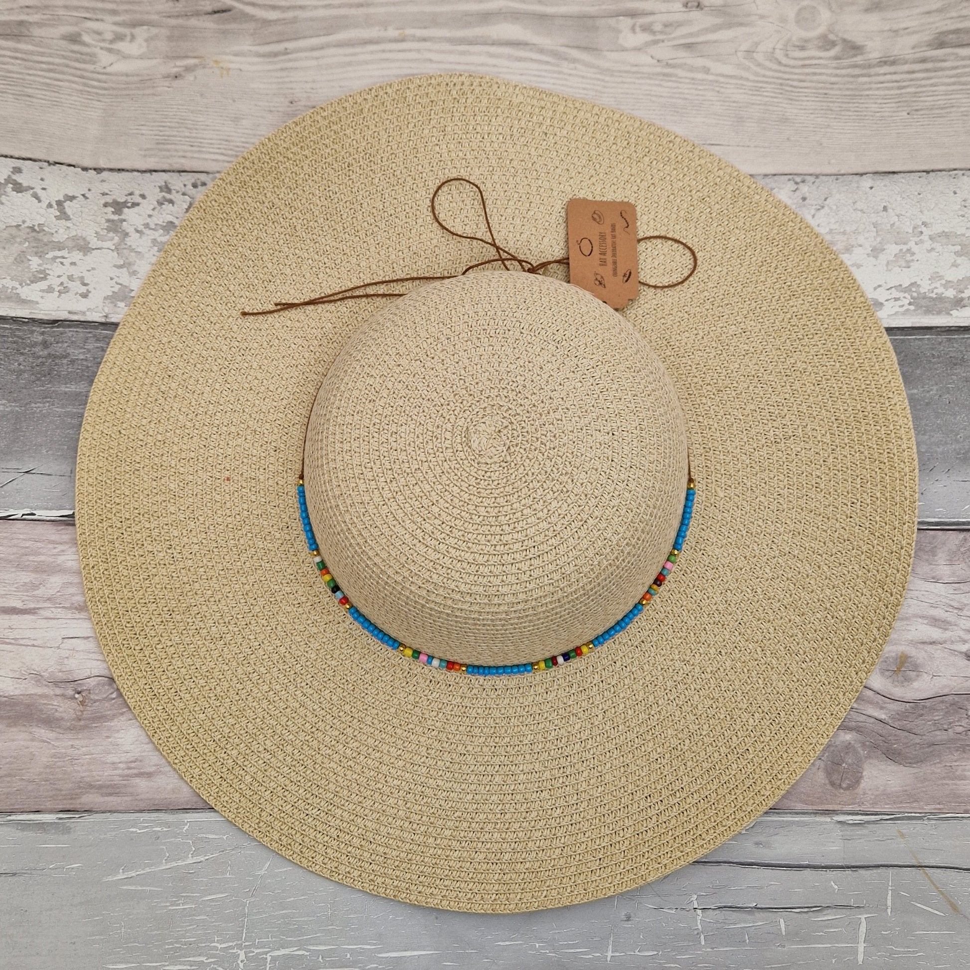 Top down view of a natural coloured wide brimmed hat with a cord around the crown covered in predominantly blue beads. 