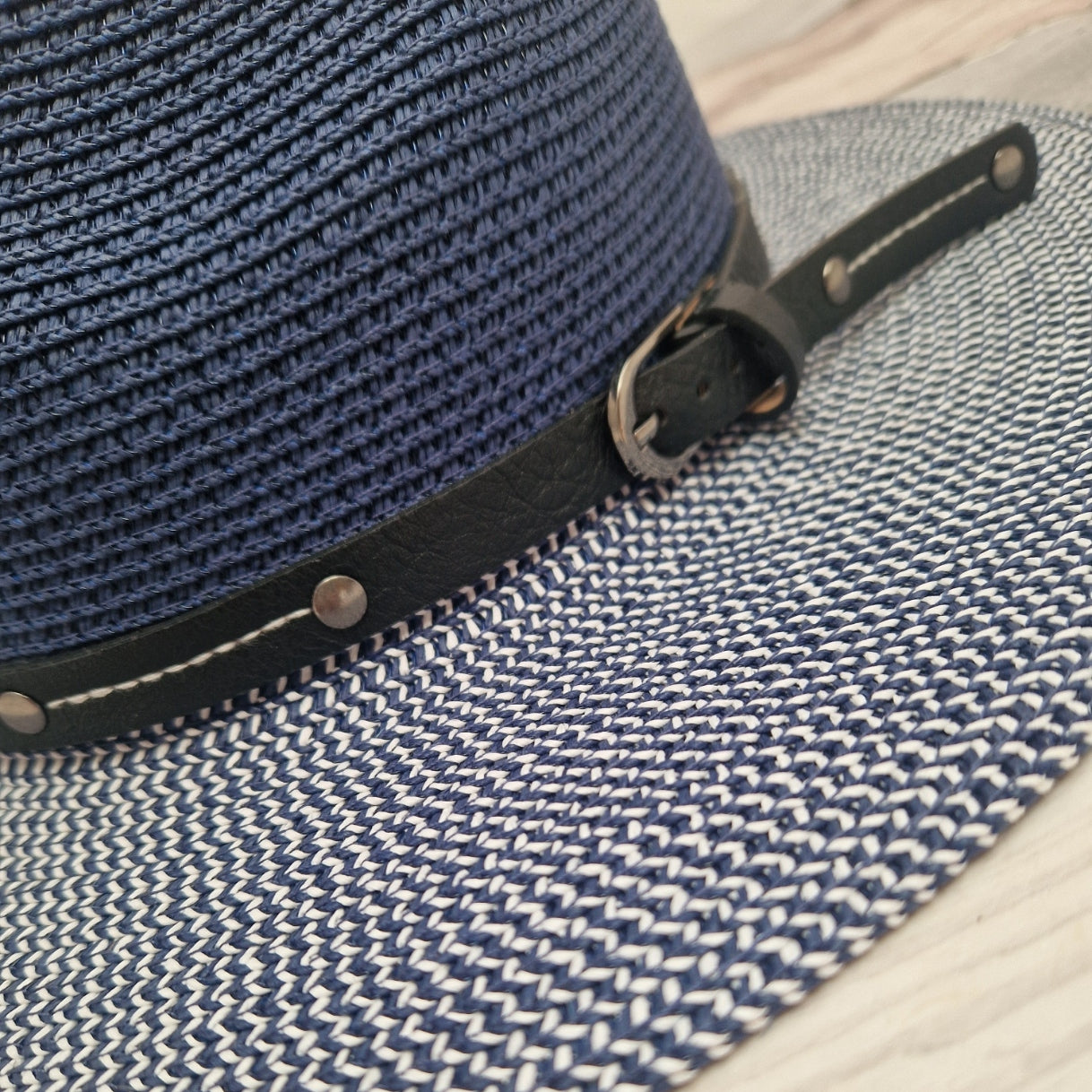 Close-up of a woven blue and white Panama hat with a black leather band and silver buckle.