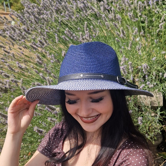 A woman wearing a blue woven Panama hat with a black band and silver buckle, posing outdoors in front of a field of lavender.