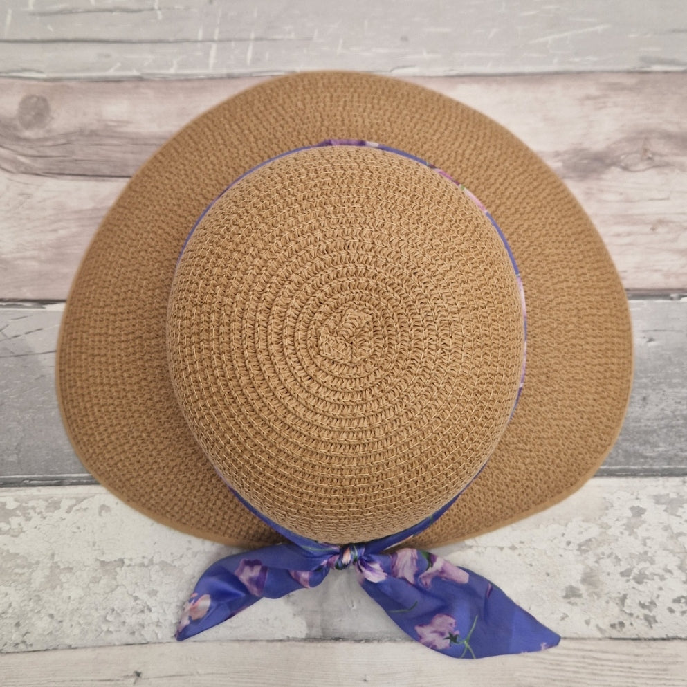 Top down view of a beige coloured backless bonnet with a purple floral ribbon band.