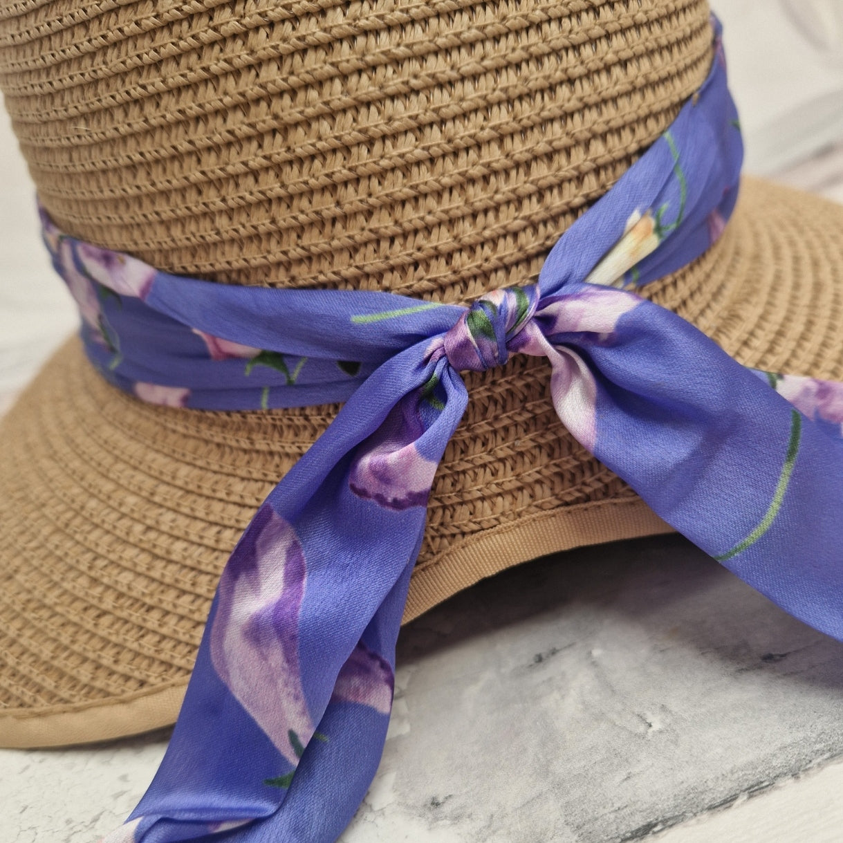 A close up view of a beige coloured backless bonnet with a purple floral ribbon band.