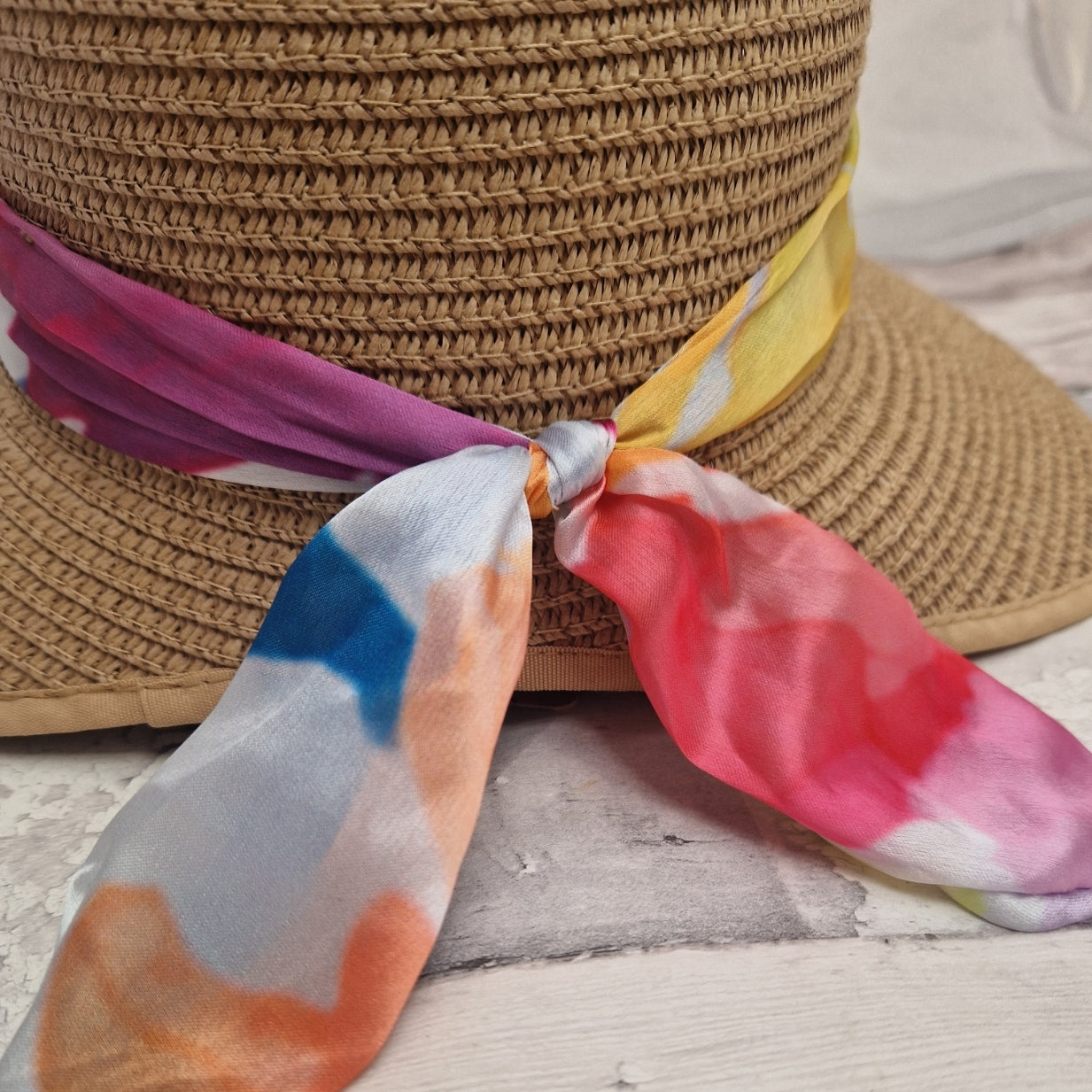 Close up view of a  beige coloured backless bonnet with a rainbow coloured ribbon band.