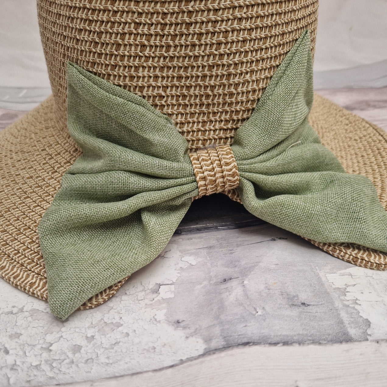 Close up shot of a backless bonnet in natural biscuit colour, finished with a large green bow across the back.