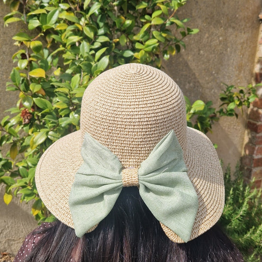 Lady wearing a backless bonnet in natural biscuit colour, finished with a large green bow across the back.