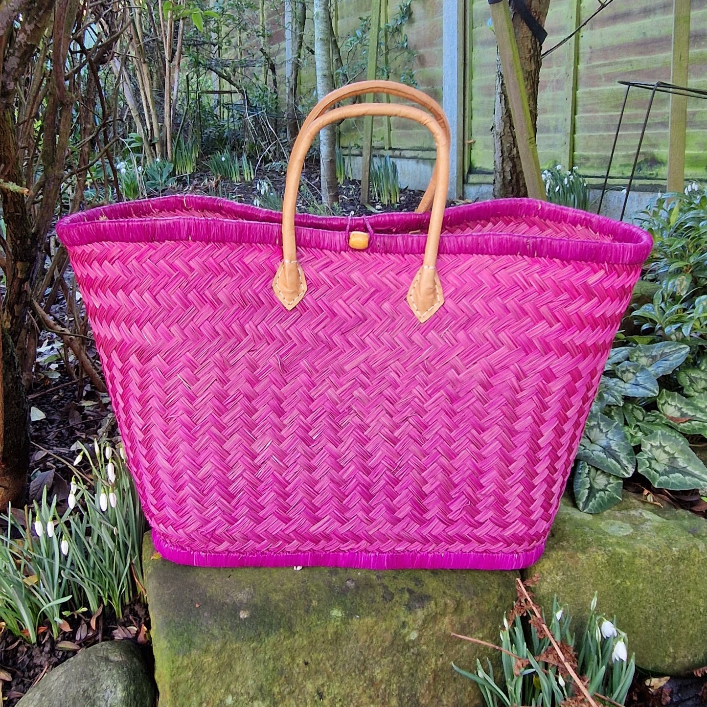 Pink woven basket with leather handles and a toggle closer.
