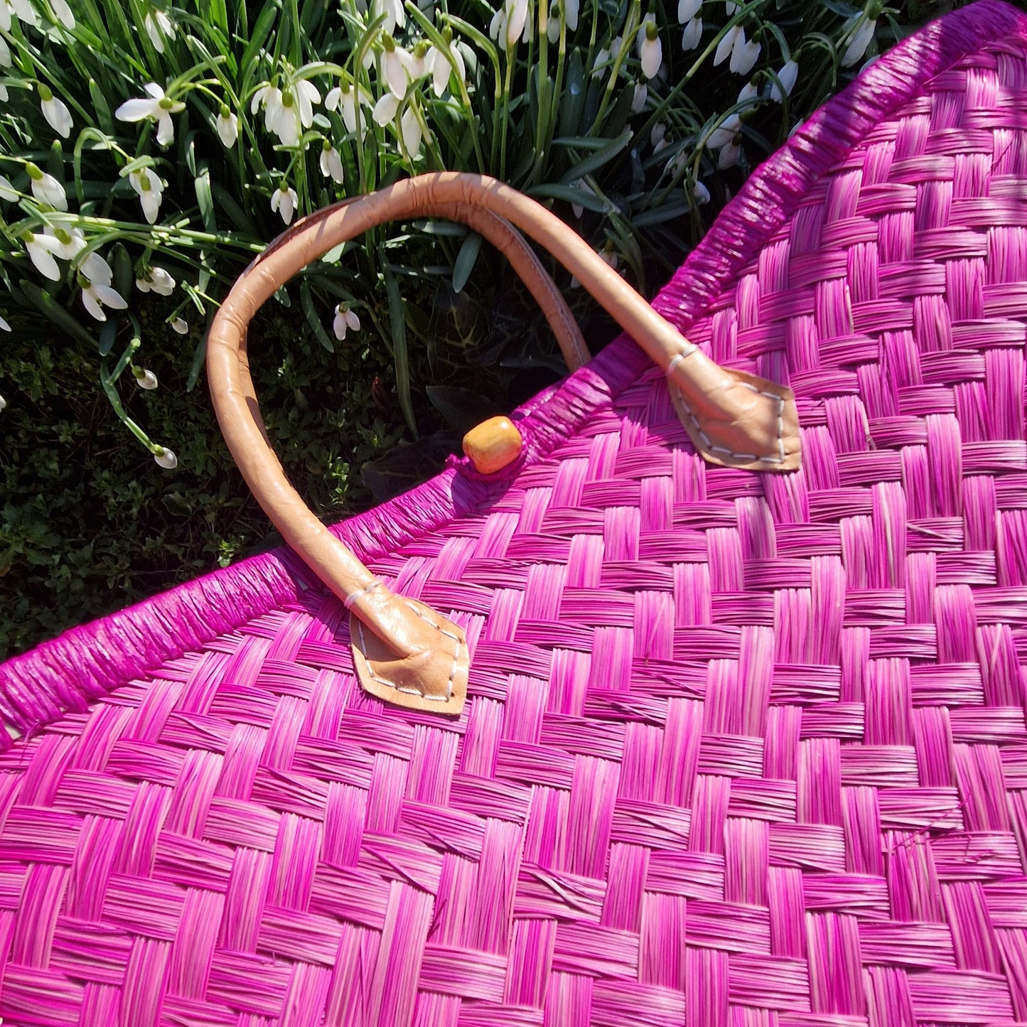 Pink woven bag with a handle on a grassy background with white flowers.
