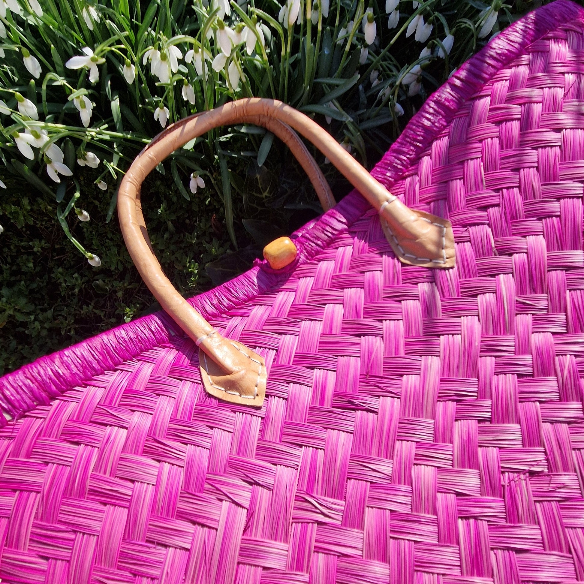 Pink woven bag with a handle on a grassy background with white flowers.