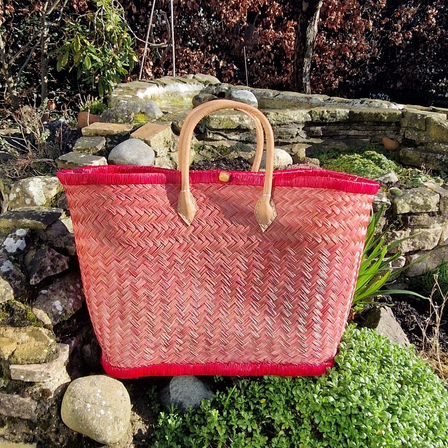 Red woven basket with leather handles and a toggle closer.