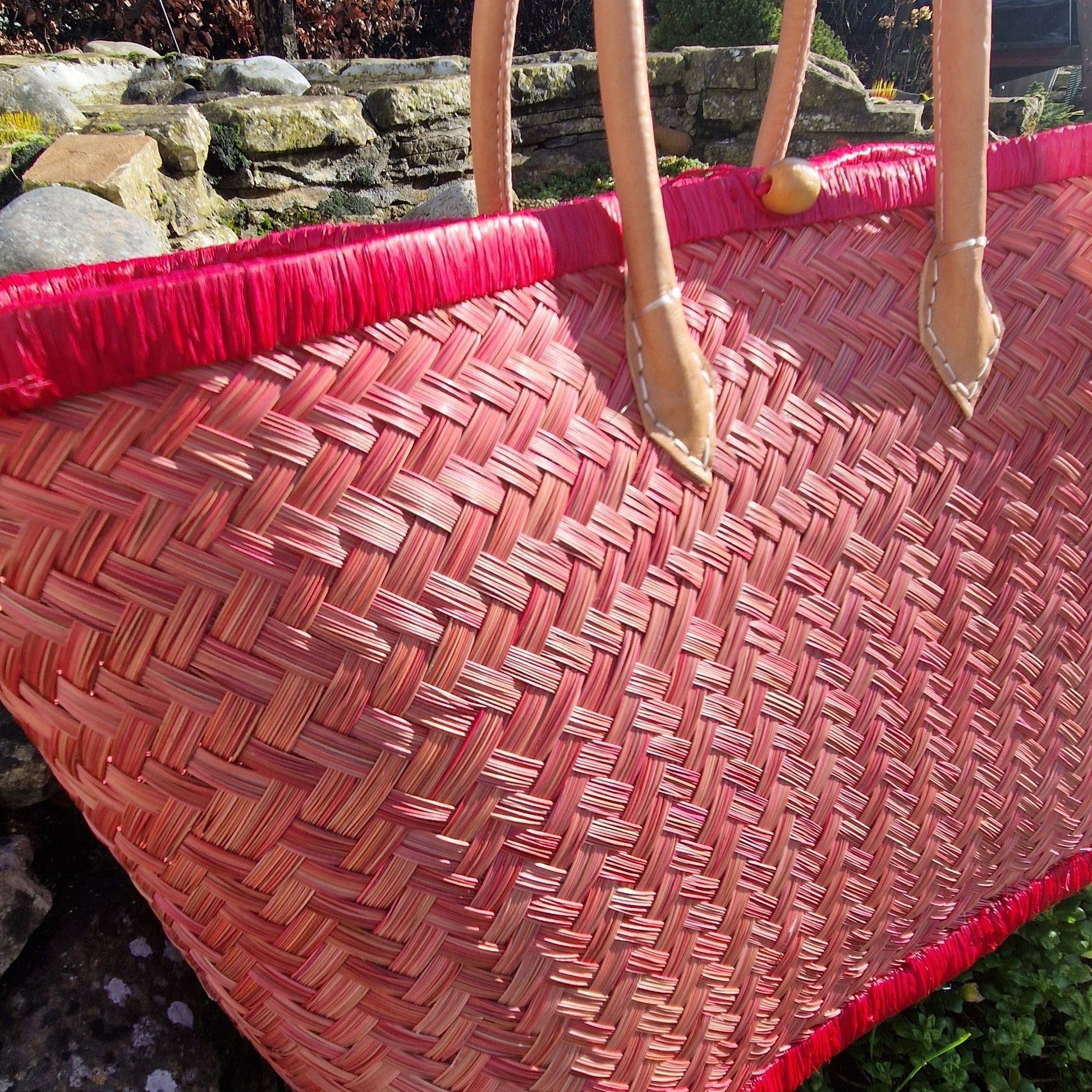 Close-up of a red woven bag with a stone wall and greenery in the background