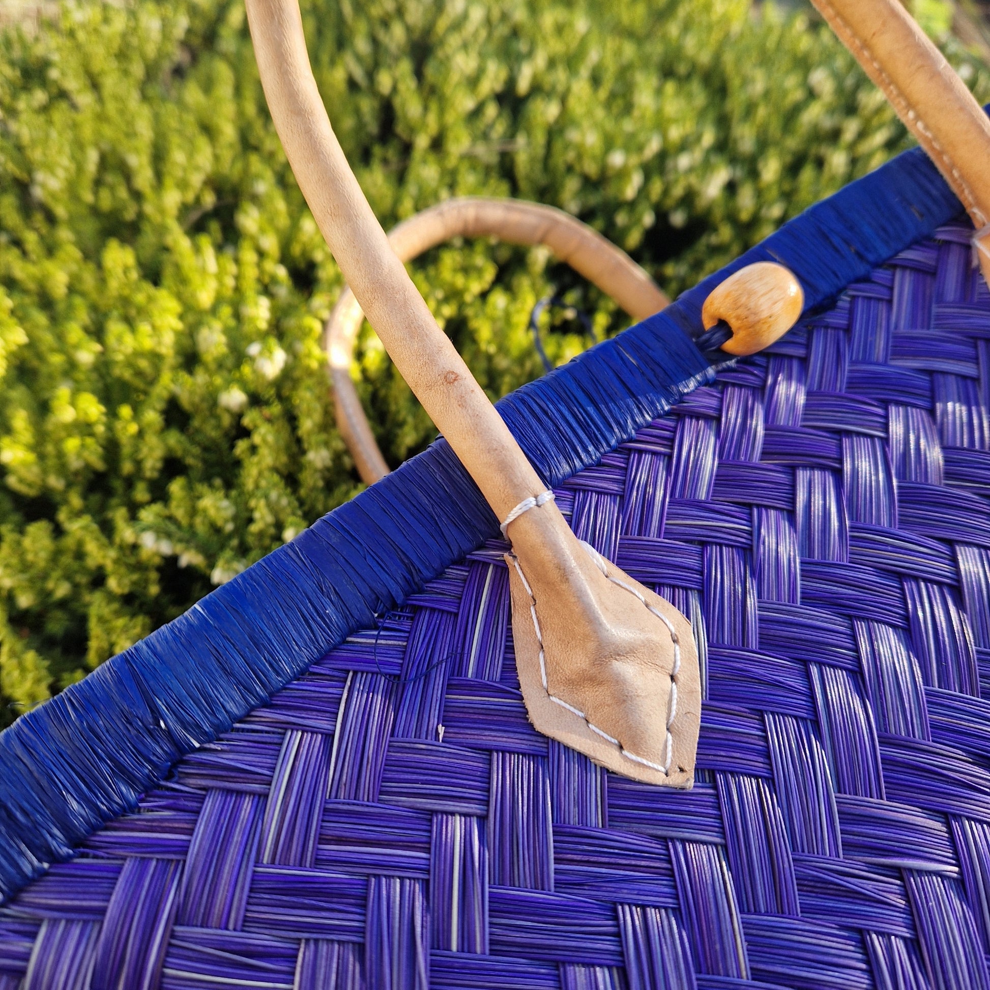 Close-up of a woven basket with a blue handle and wooden spoon against a blurred green background