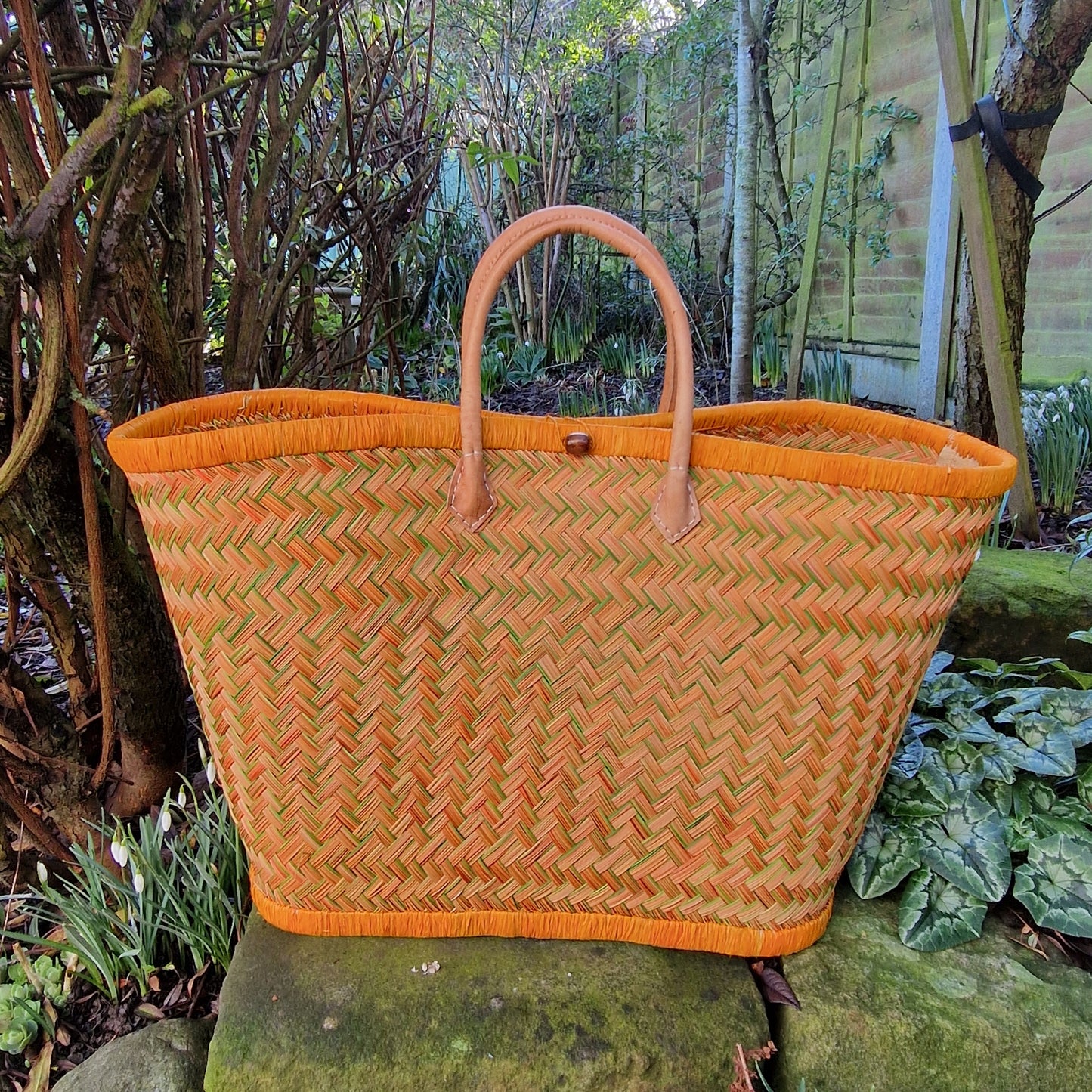 Woven basket with orange and green pattern and a leather handle.