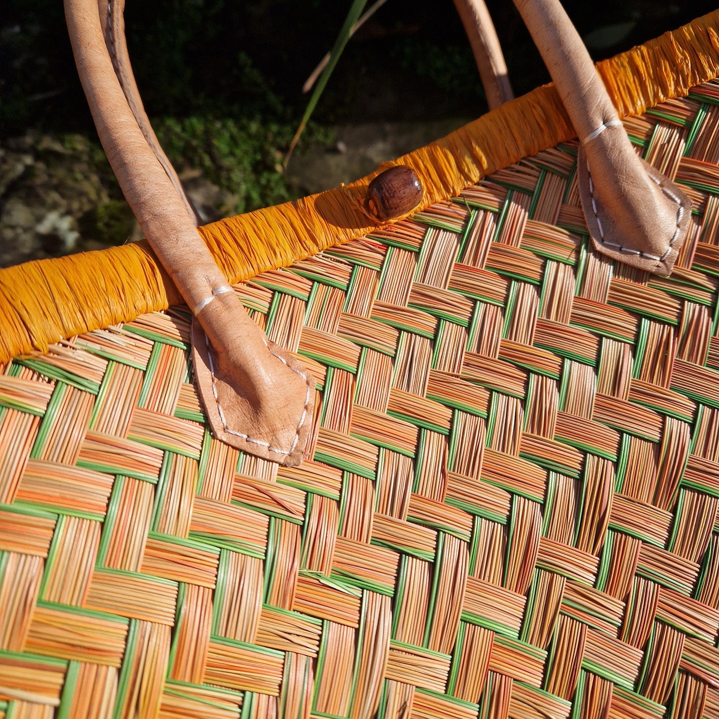 Close-up of a woven basket with an orange and green pattern and a leather handle.
