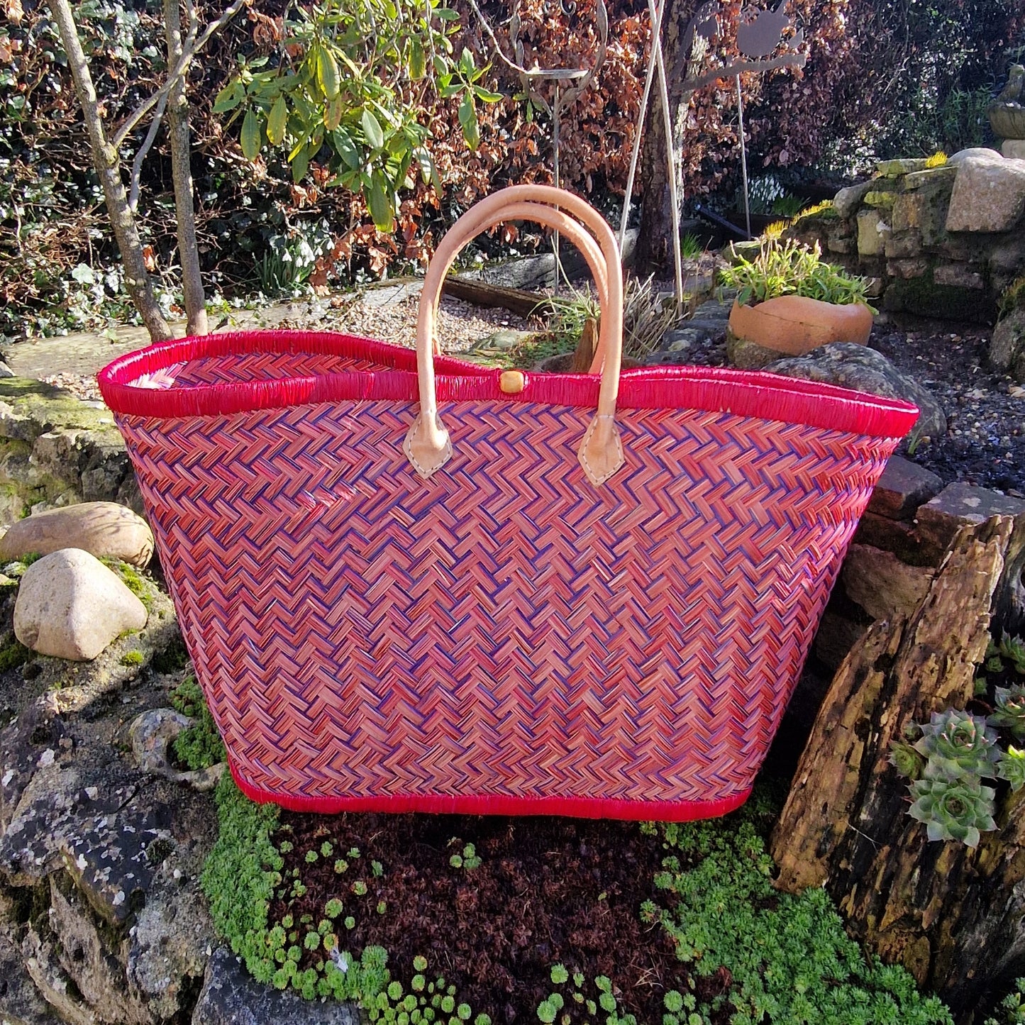 Woven basket with red and blue pattern and a leather handle.