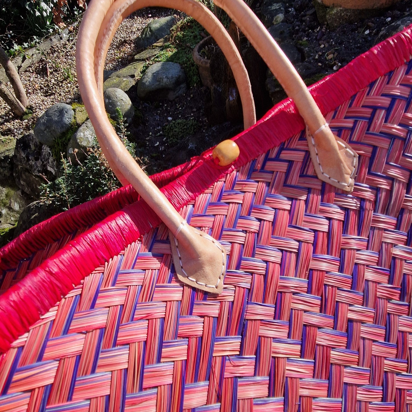 Close-up of a woven basket with red and blue pattern and a leather handle.
