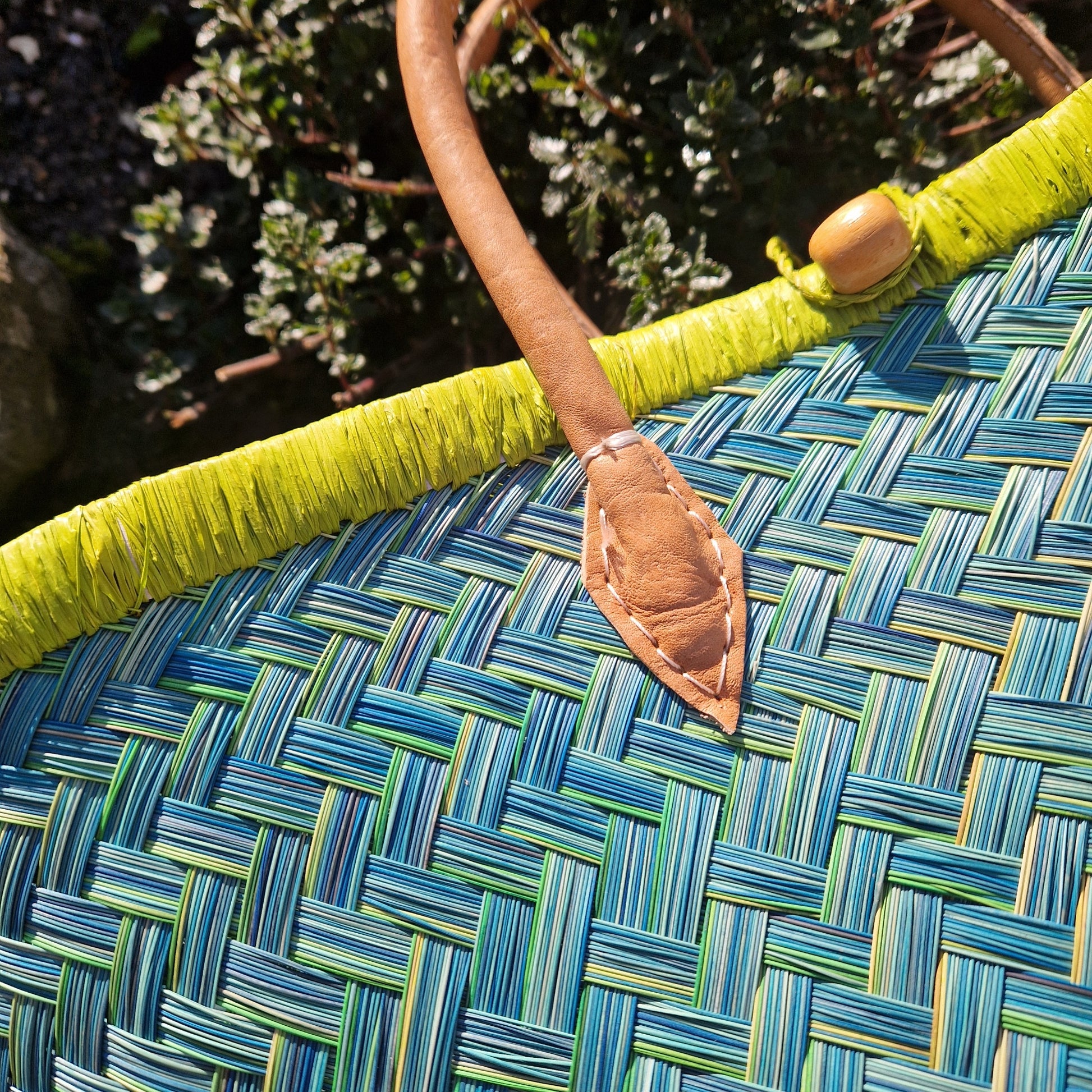 Close-up of a woven basket with green and blue pattern and a leather handle.