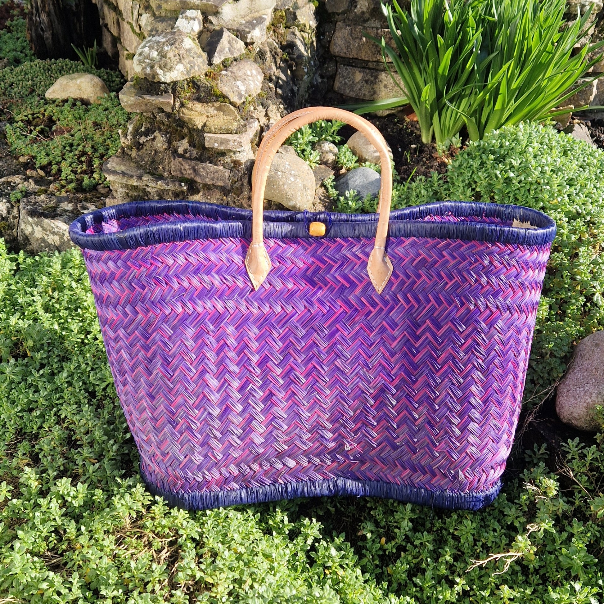 Woven basket with pink and blue pattern and a leather handle.