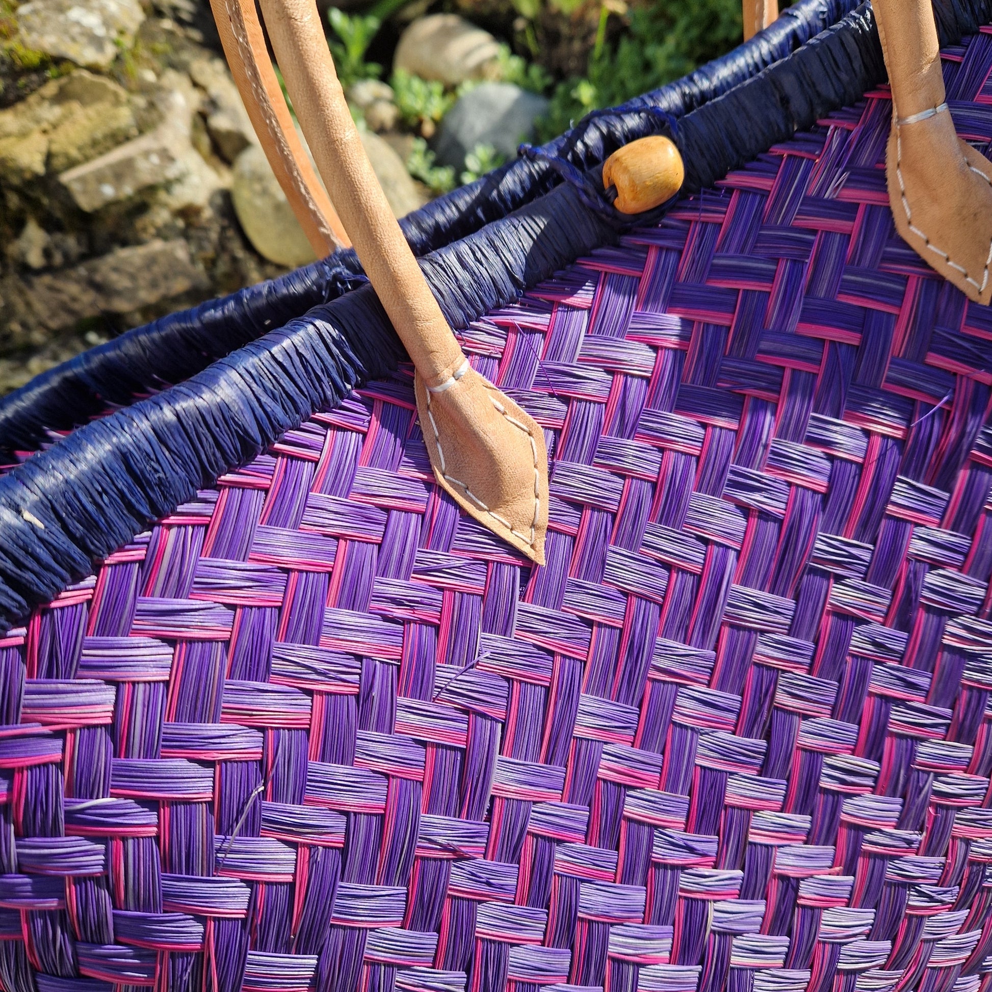Close-up of a woven basket with pink and blue pattern and a leather handle.