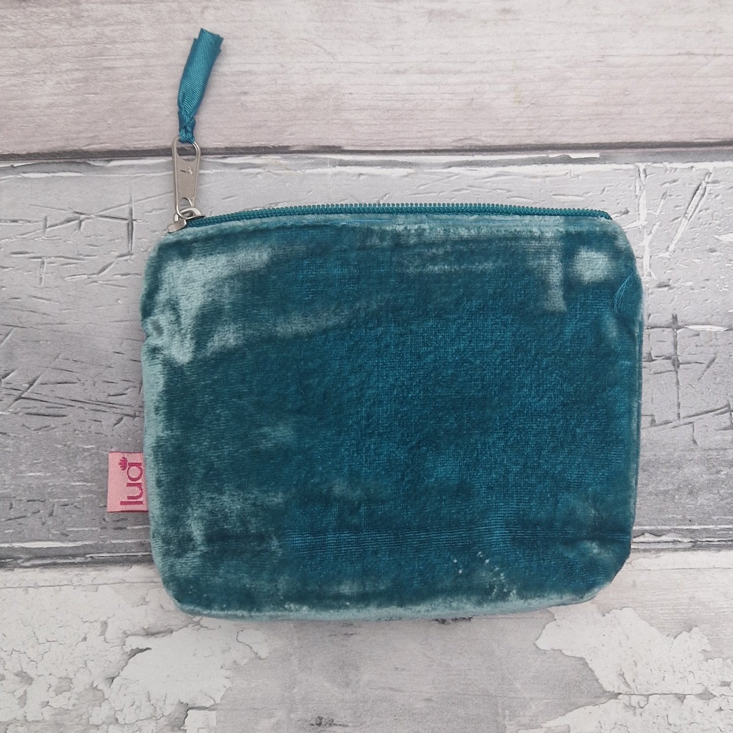 Teal velvet pouch with a pink tag on a textured gray surface