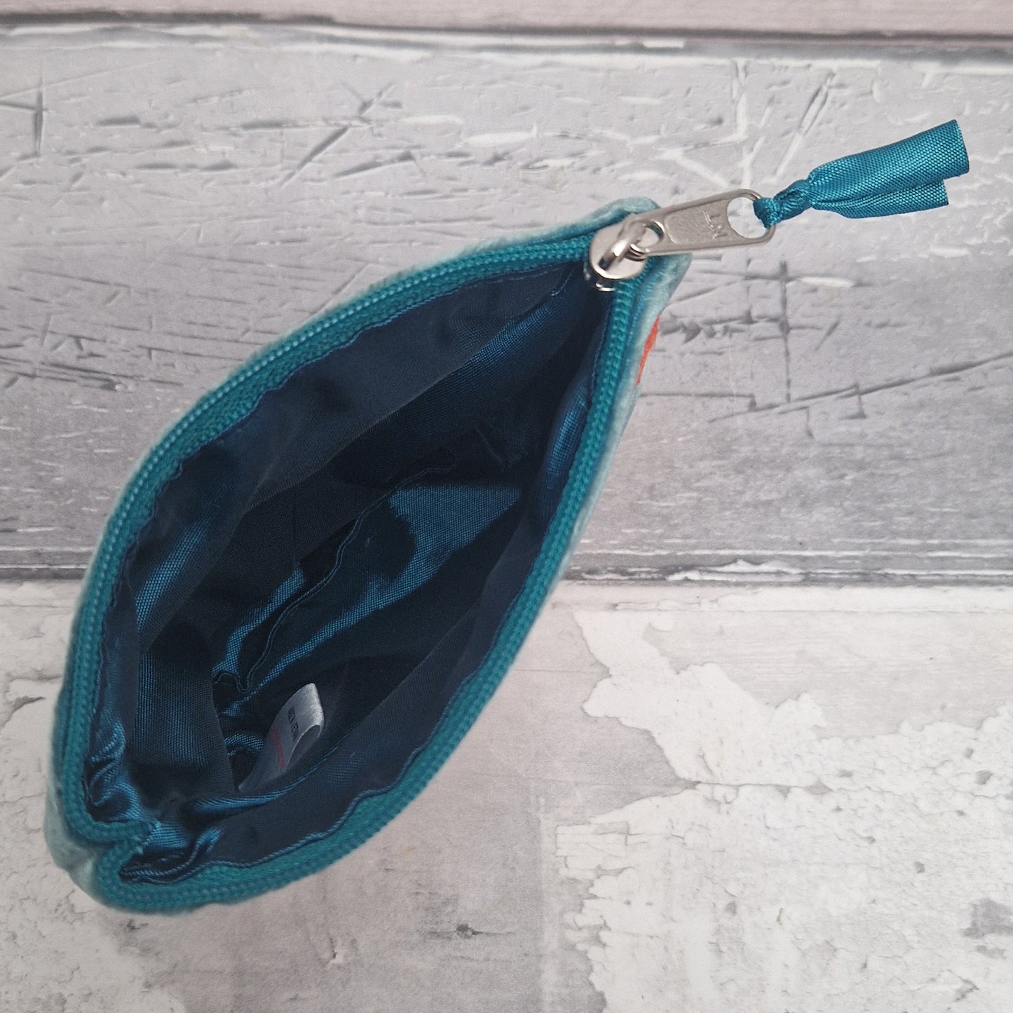 Teal pouch with a zipper on a textured gray surface