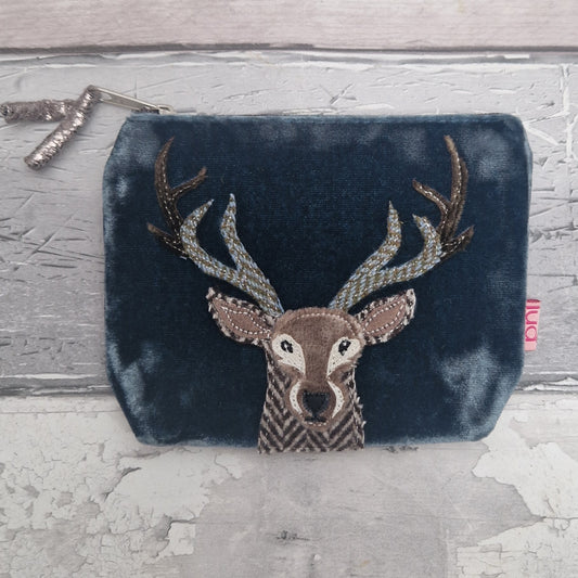 Blue velvet pouch with embroidered deer design on a textured surface