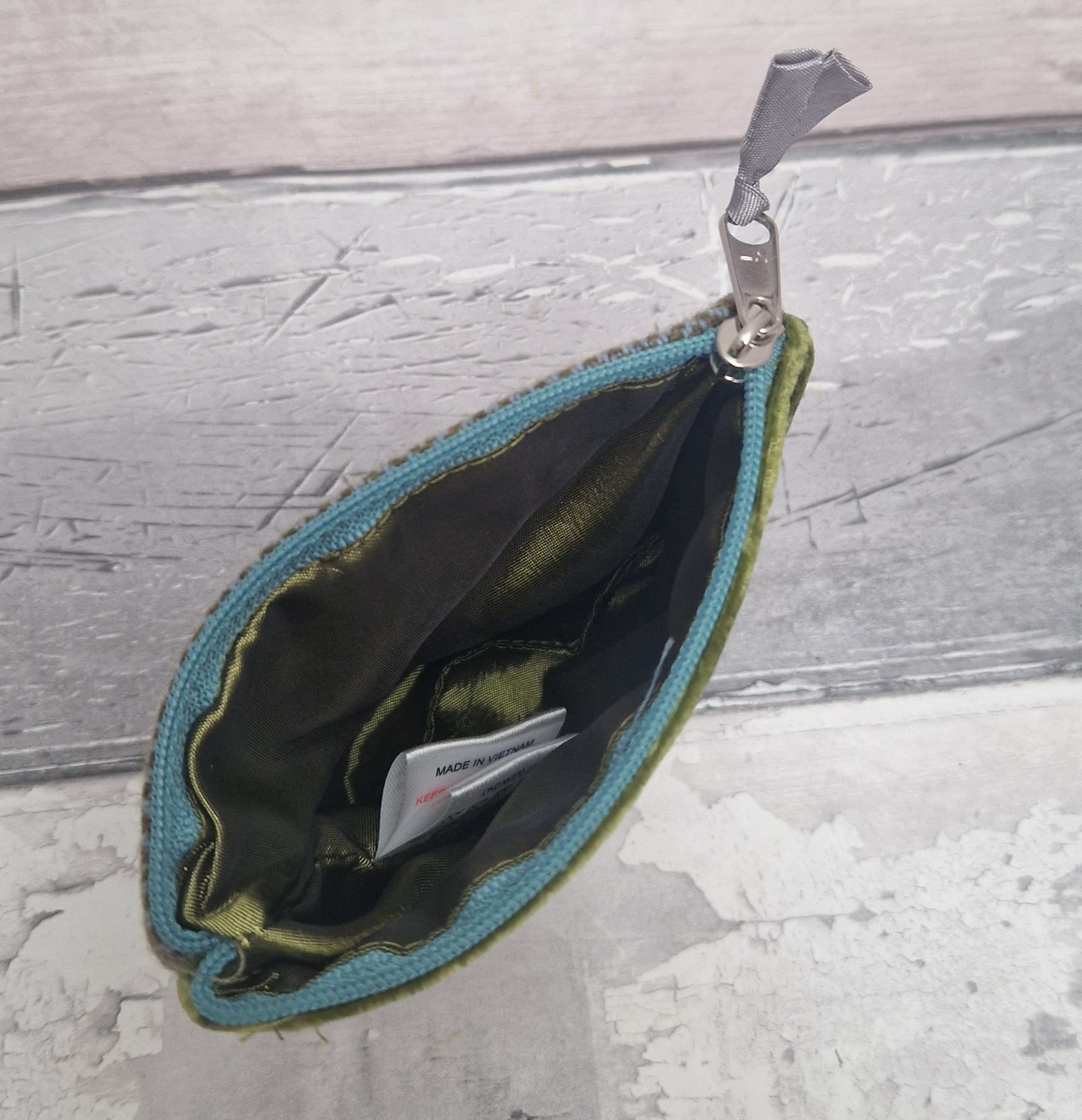 Open teal and green pouch with a card inside on a textured gray surface