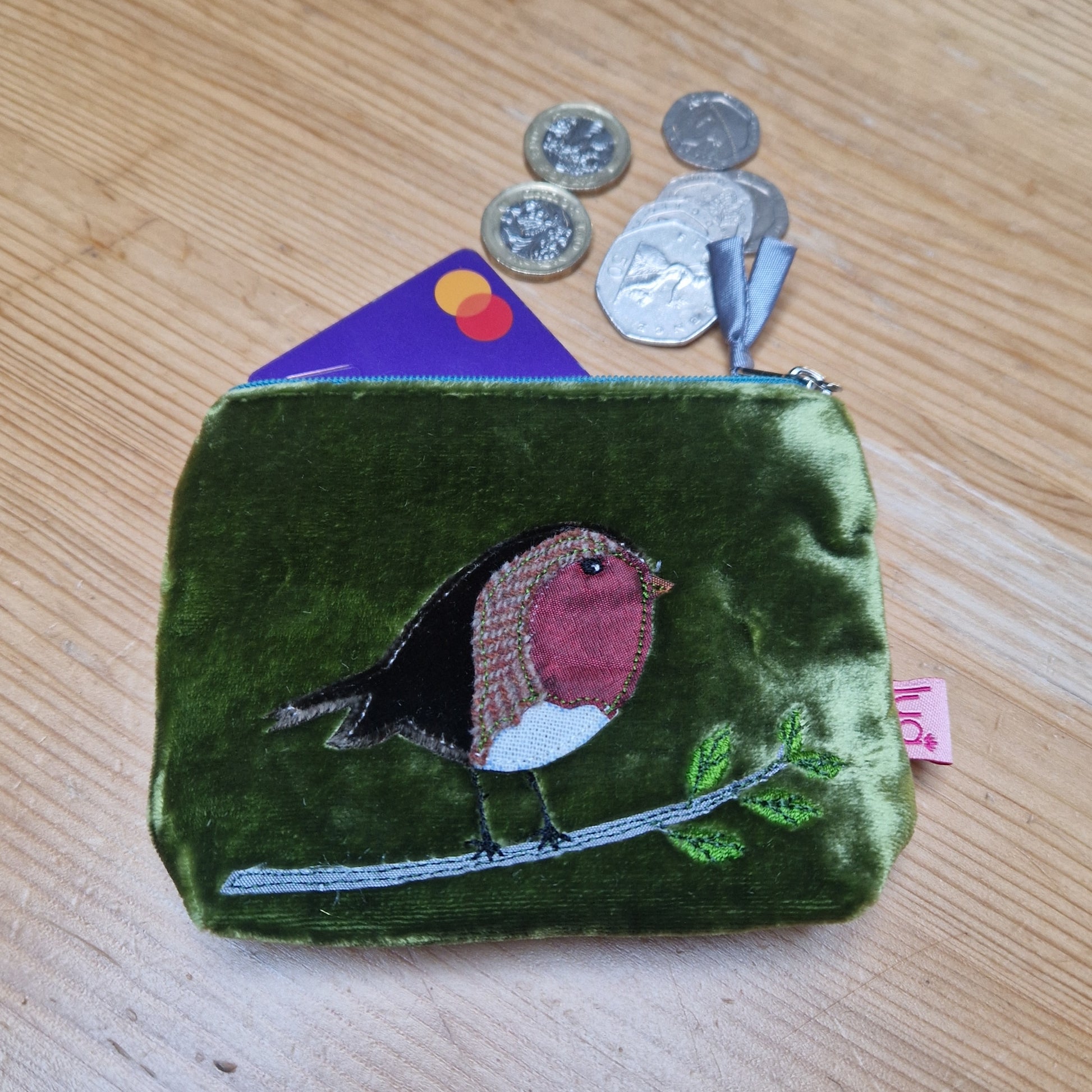 Green coin purse with a bird design on a wooden surface with coins and a card.