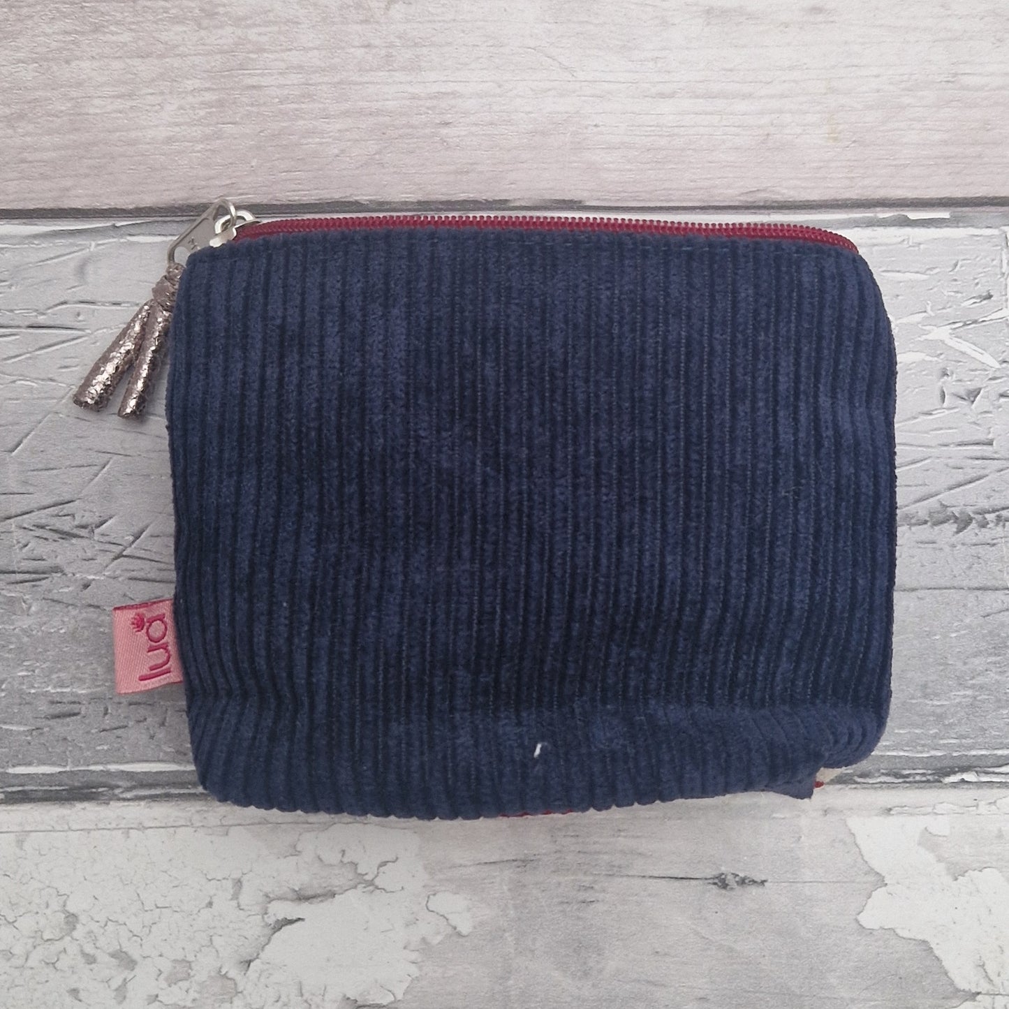 Navy blue corduroy pouch with a red zipper on a textured gray surface