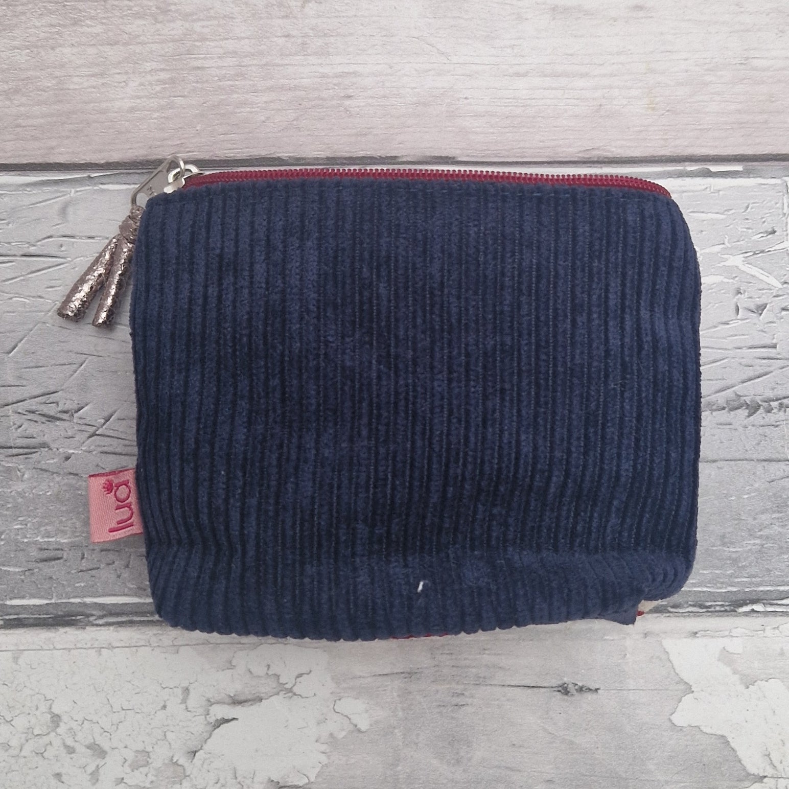 Navy blue corduroy pouch with a red zipper on a textured gray surface