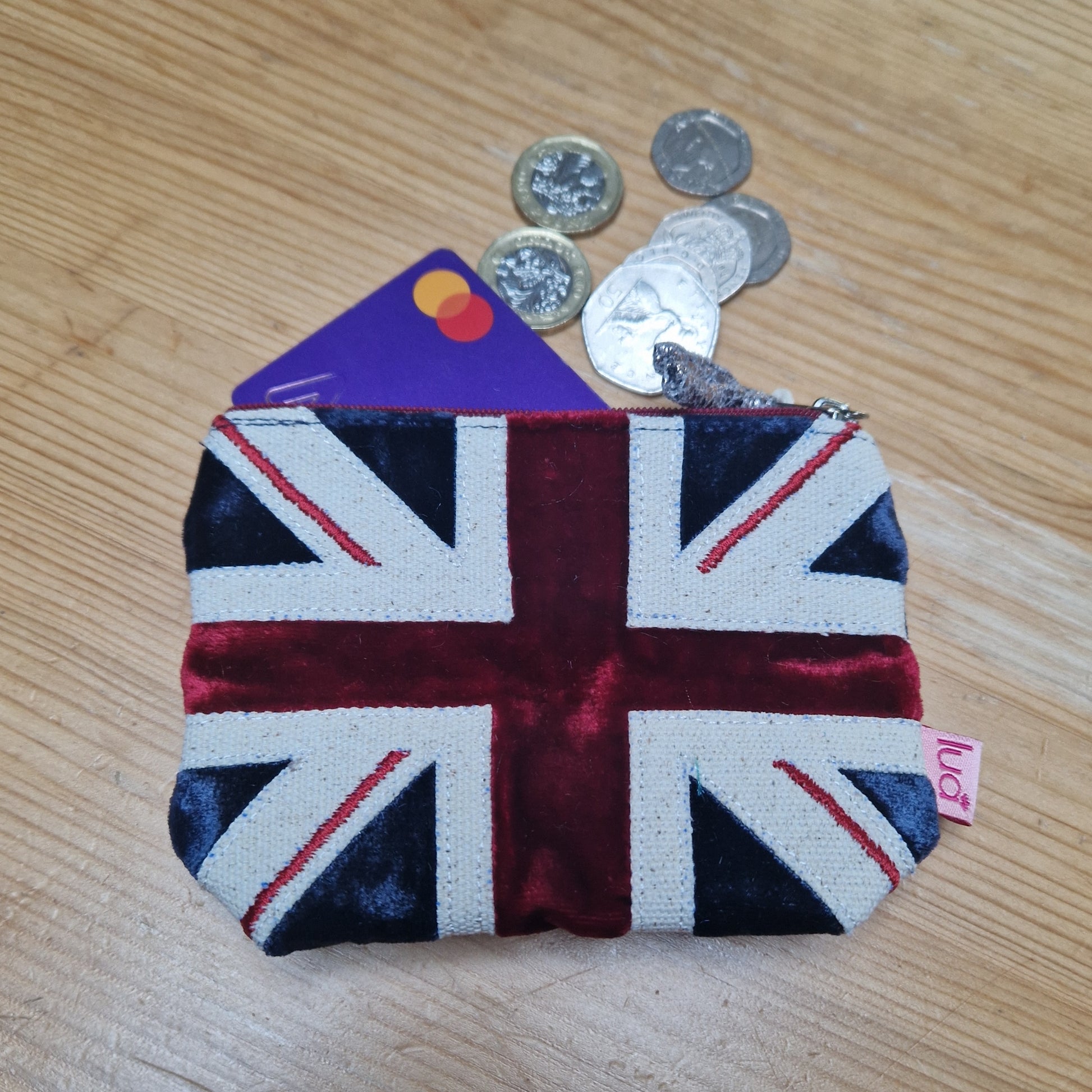 Small pouch with Union Jack design on a wooden surface with coins and cards.
