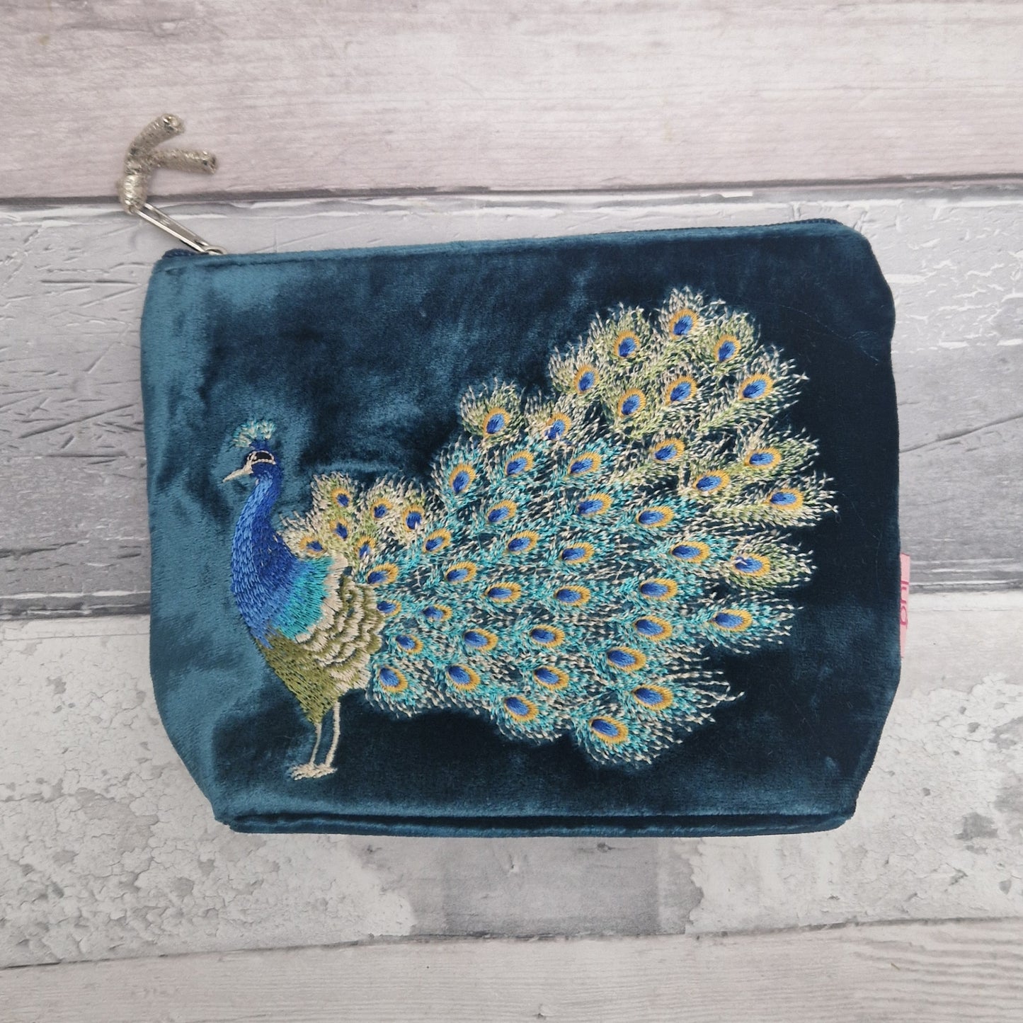 Blue velvet clutch with peacock embroidery on a wooden surface