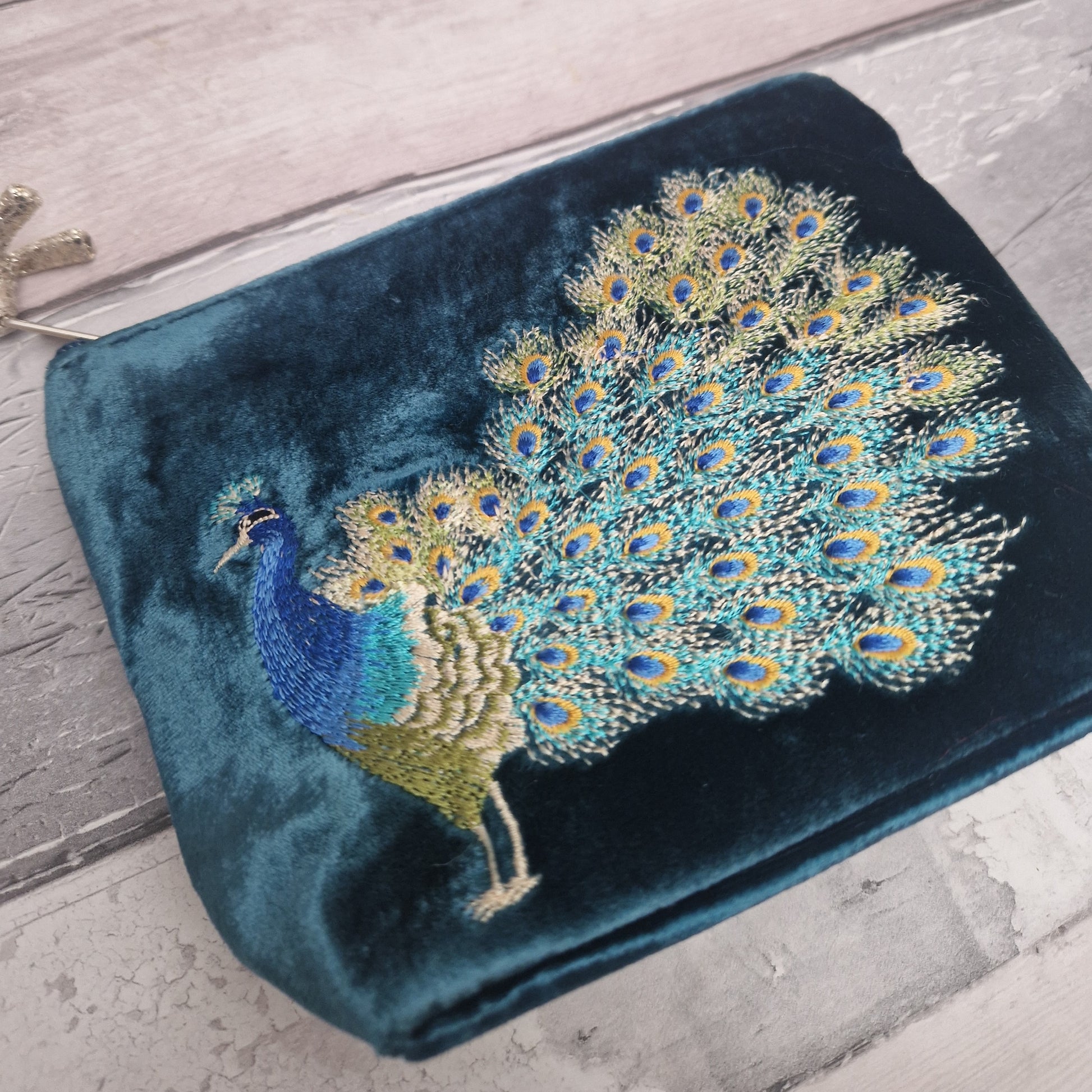Blue clutch bag with embroidered peacock design on a wooden surface