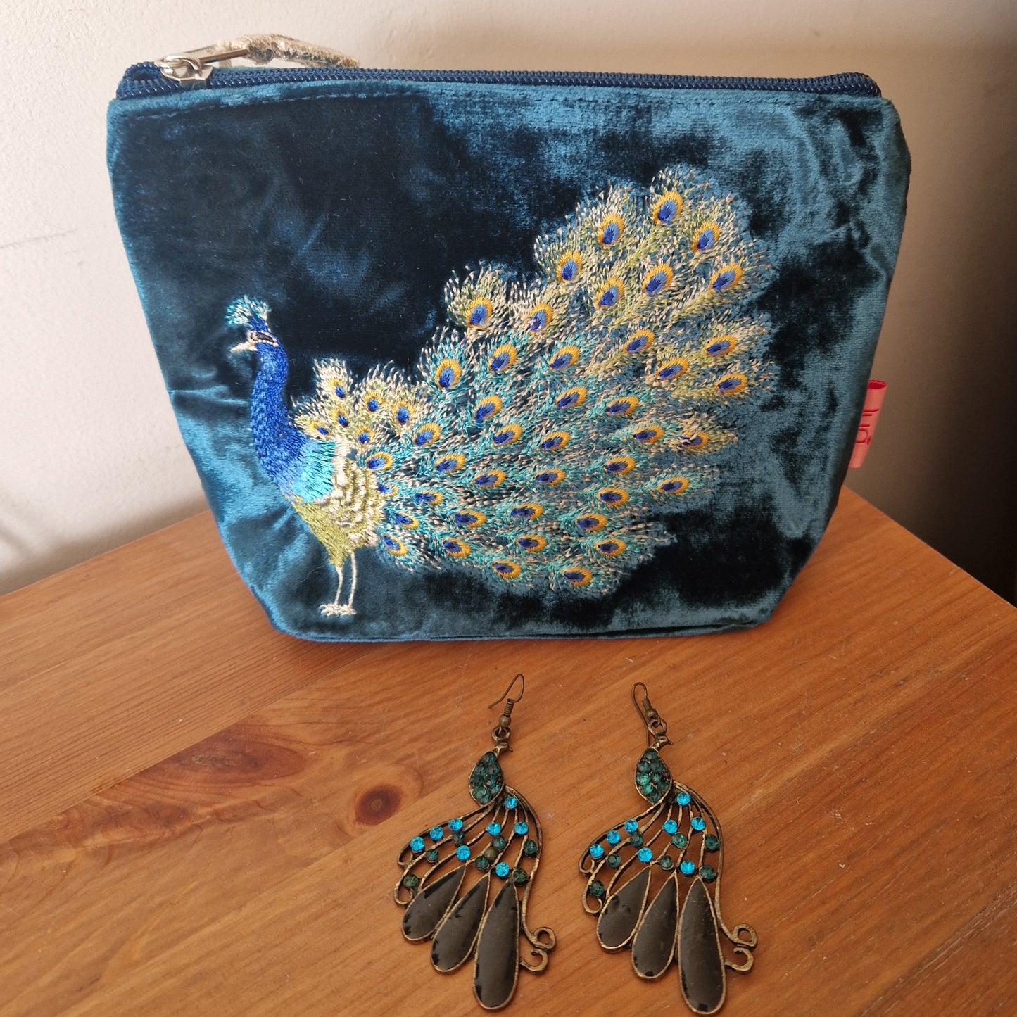 Blue velvet pouch with peacock design and matching earrings on a wooden surface
