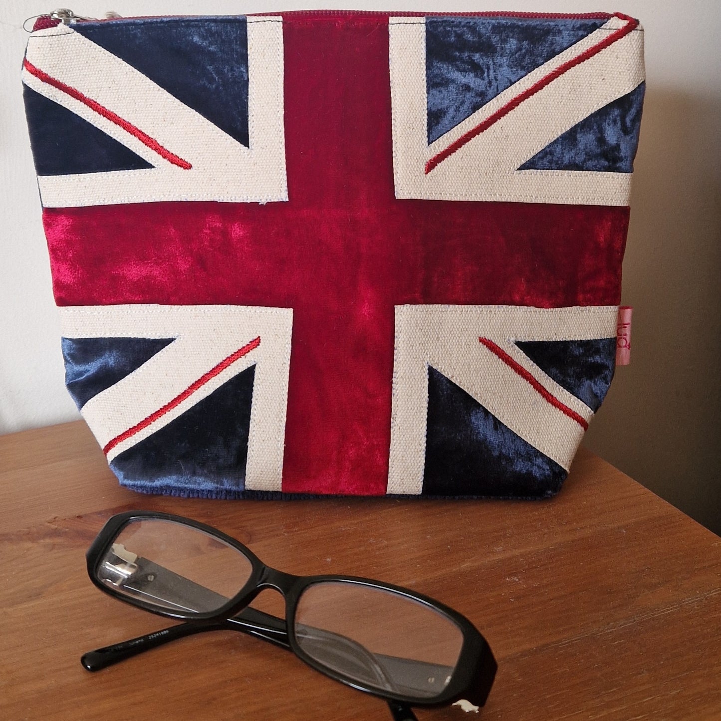 Pouch with Union Jack design on a wooden surface with glasses in front