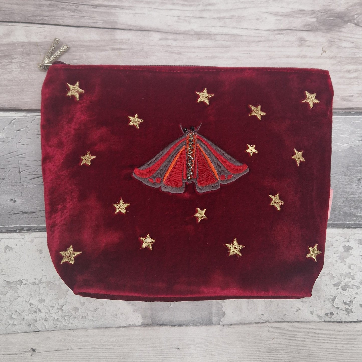 Red velvet pouch with a red moth design and gold stars on a wooden surface