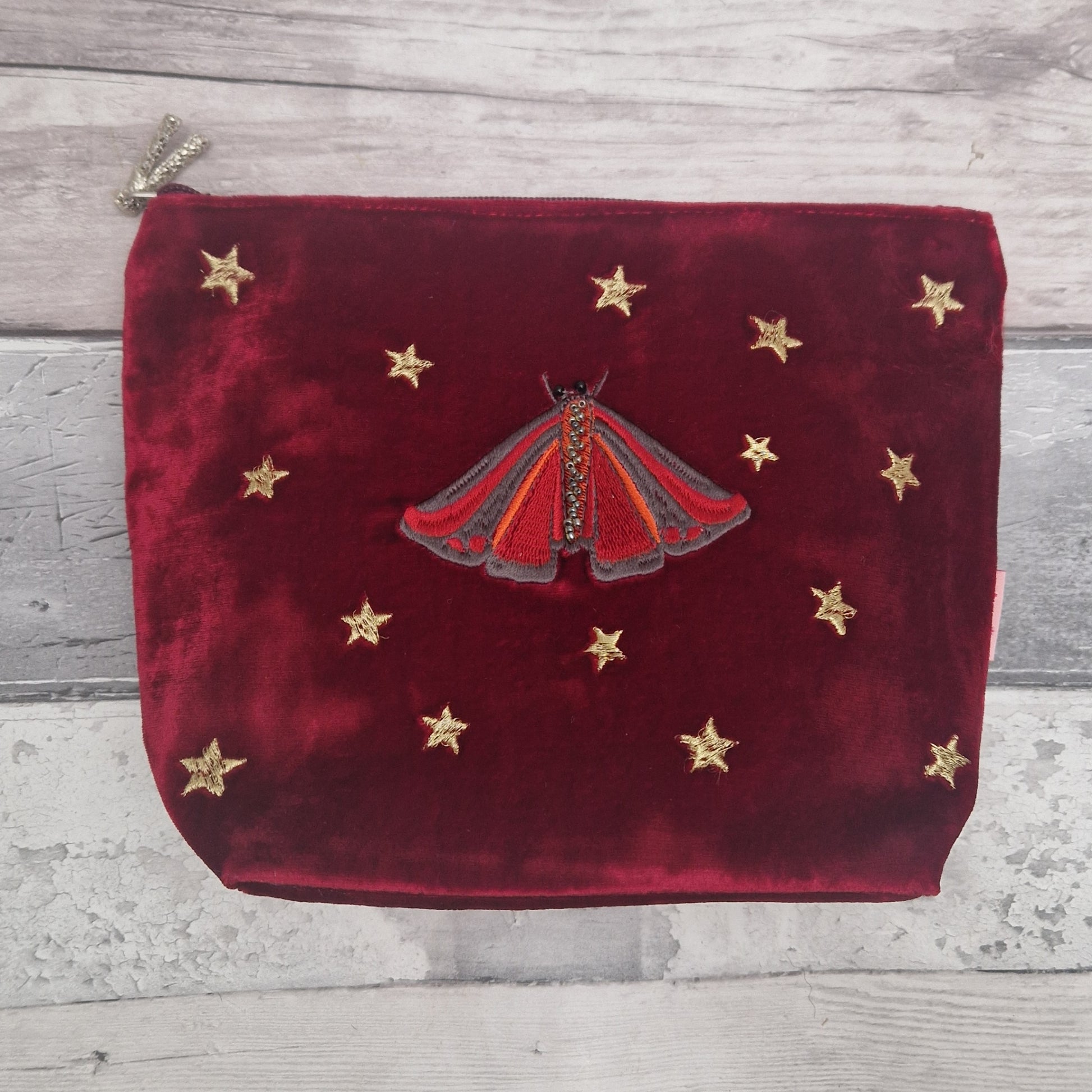 Red velvet pouch with a red moth design and gold stars on a wooden surface