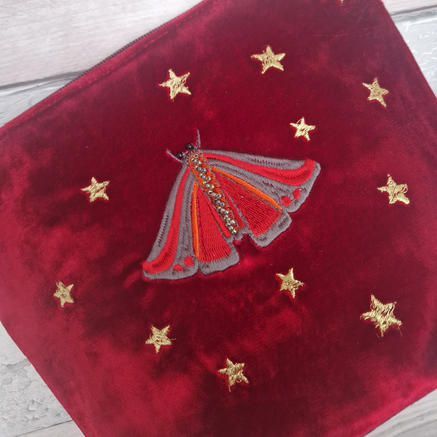 Red velvet pouch with embroidered Cinnabar Moth and gold stars on a wooden surface.