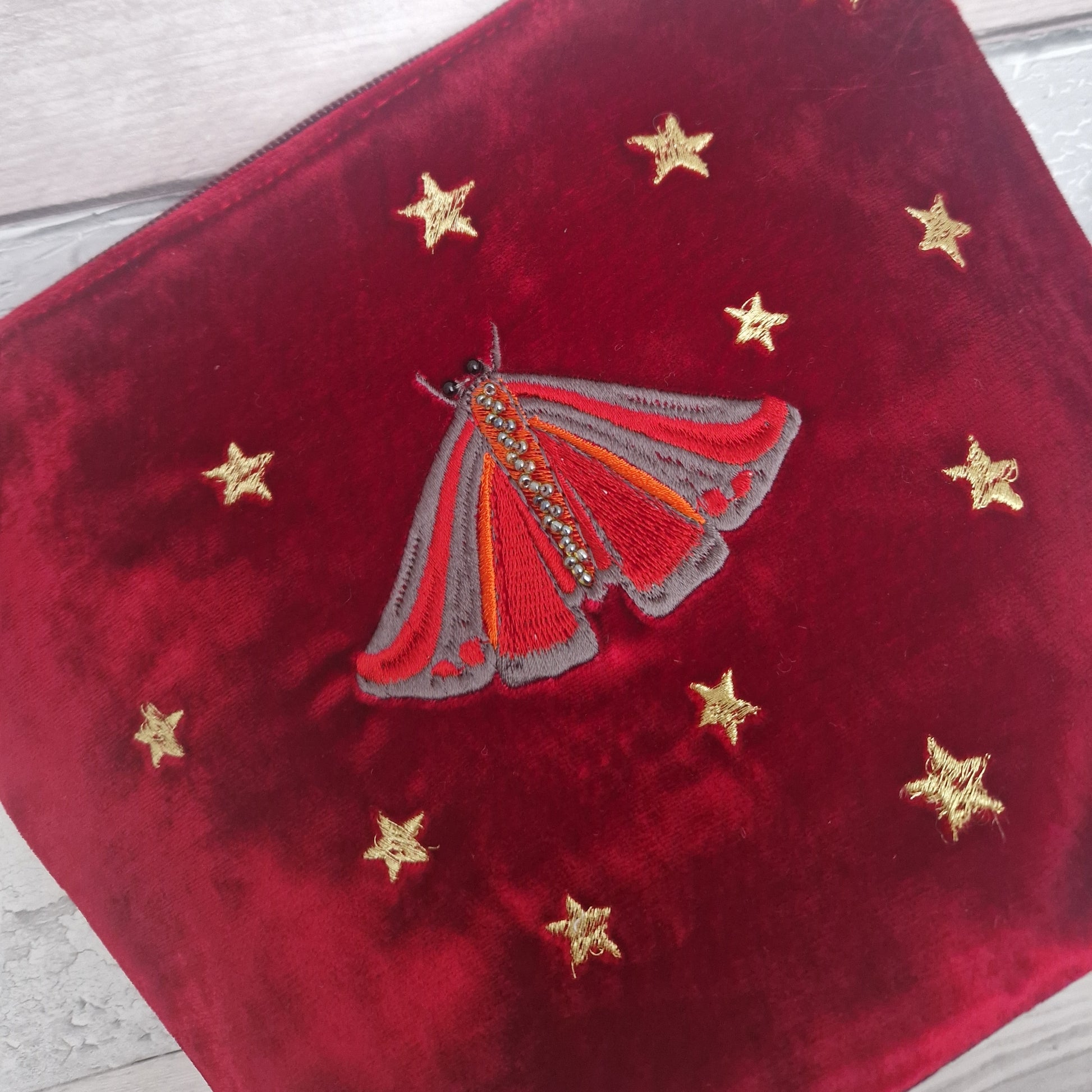 Red velvet pouch with embroidered Cinnabar Moth and gold stars on a wooden surface.