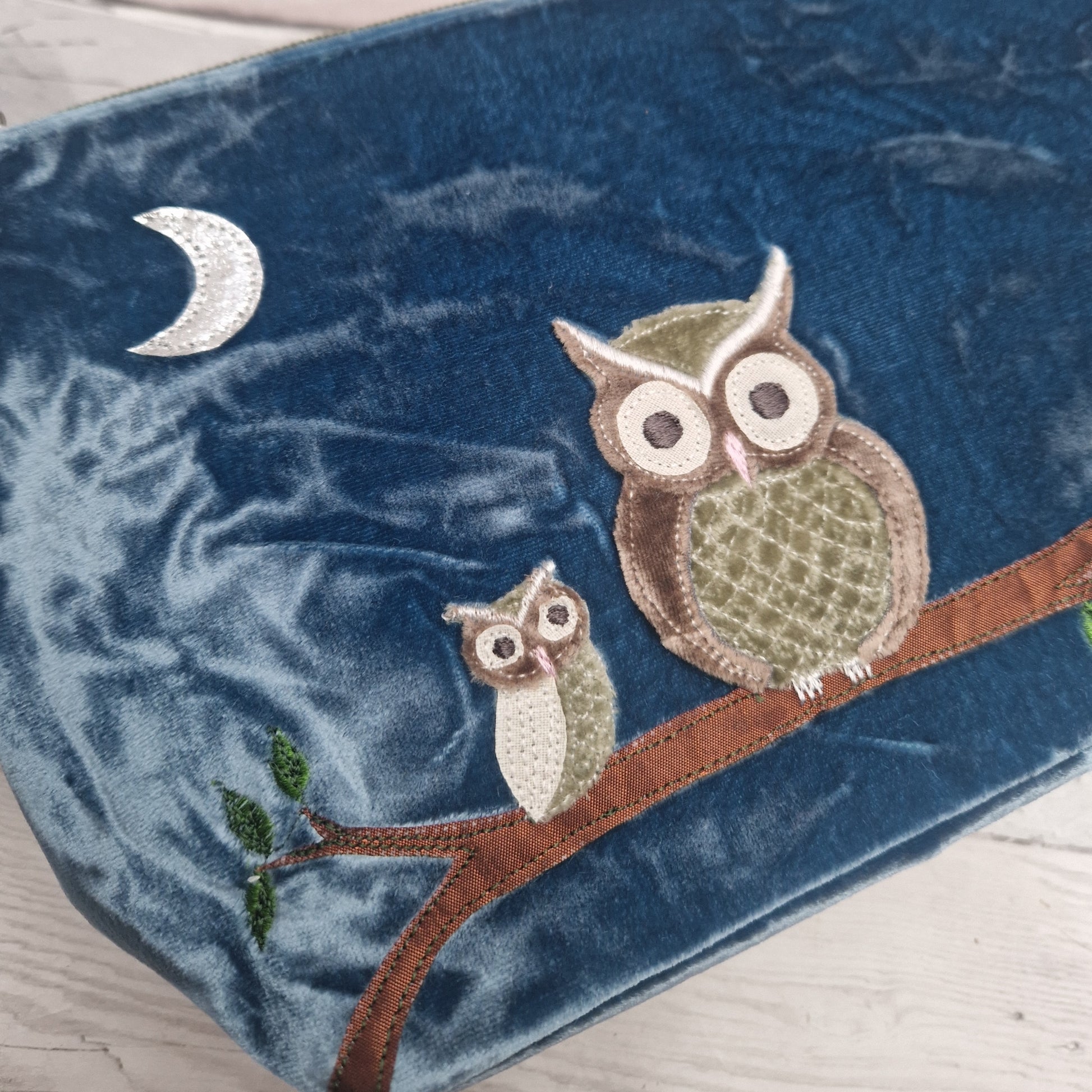 Embroidered owls on a branch with a crescent moon on a blue fabric background
