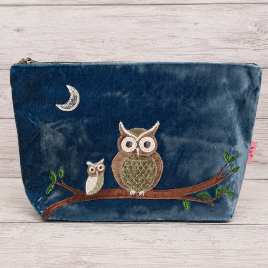 A navy blue velvet pouch featuring an embroidered design of two owls on a branch under a crescent moon, set against a light wood background.